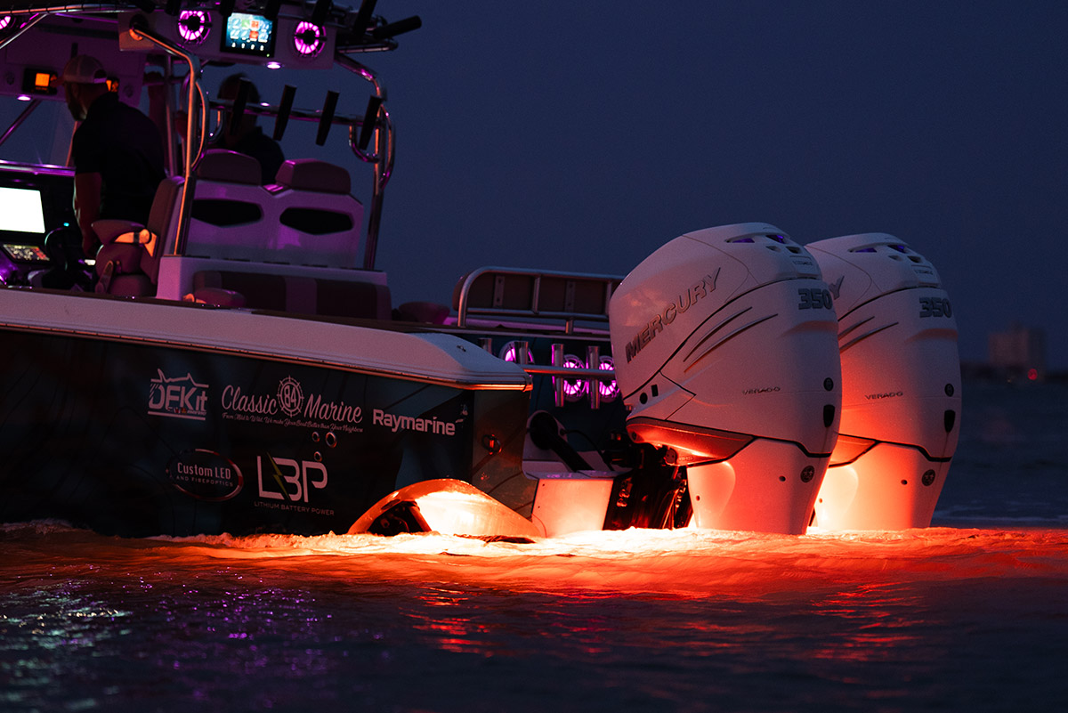 The stern of a sports fishing boat with bright red underwater lights from Shadow-Caster illuminating the engines.